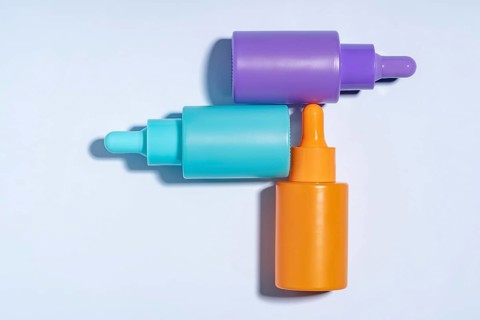 Top view of three vibrant serum bottles in purple, turquoise, and orange colors, designed with