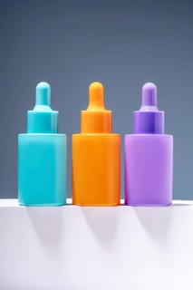 Three vibrant and colorful serum bottles aligned on a sleek surface with a soft gray gradient