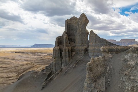 A towering rock formation emerges from the expansive desert landscape under a cloudy sky in