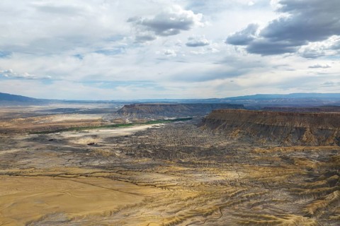 Aerial view of a rugged desert landscape under a dramatic, cloud filled sky in Hanskville, Utah.