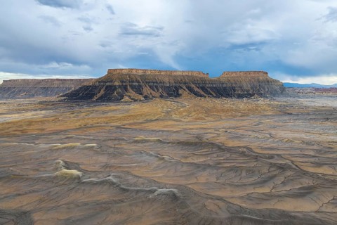 A breathtaking view of a desert plateau rising under a vast, cloudy sky, showcasing layers of