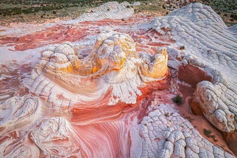 Aerial view of swirling rock formations in vibrant reds and whites in White Pocket, showcasing the