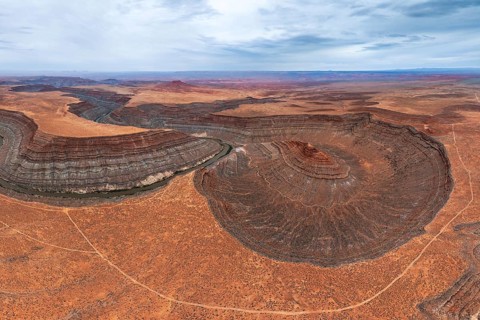 An aerial view showcases a river elegantly meandering through layered rock formations in a vast San