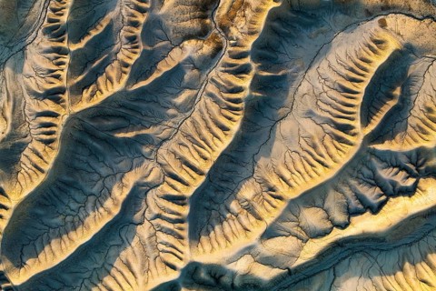 Aerial view highlighting Caineville Mesa's intricate desert patterns. Sunlight casts a warm golden