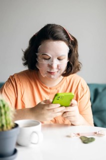 Woman at home, wearing facial beauty mask while browsing on her smartphone. A peaceful self-care