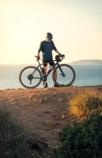 Male cyclist holding his road bike and gazing at the sea during sunset in Zahara de los Atunes,