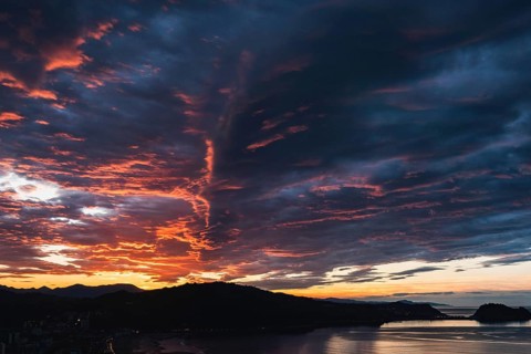 Breathtaking view of vibrant sunset skies above rolling hills framing a serene coastal backdrop,