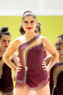 A confident gymnastic whit disability in a burgundy outfit adorned with rhinestones stands onstage