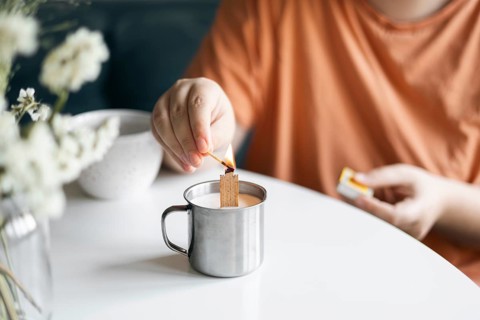 Cropped view of unrecognizable woman in a tangerine top lighting a candle inside a metal mug,