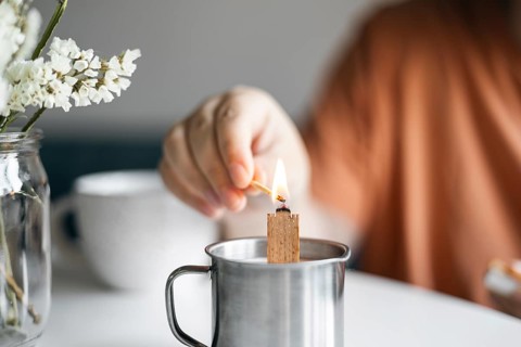 Cropped unrecognizable woman lights a candle placed in a metal mug, creating a cozy atmosphere at