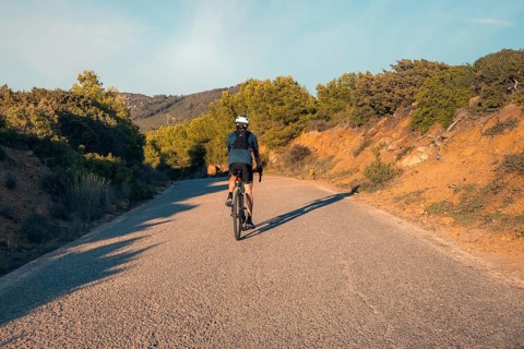 Back view of an unrecognizable male cyclist riding on a quiet road through the hills near Faro