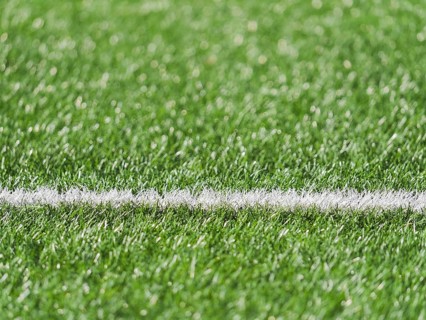 A close up image showcasing the lush green grass of a soccer field with a crisp white line marking.