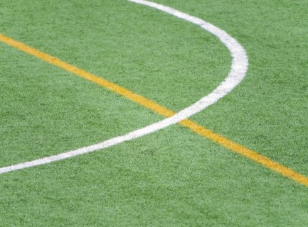 A close up of white and yellow lines marking a soccer field on artificial green turf. The detailed