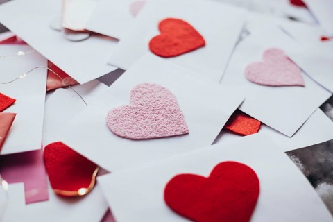 A variety of red and pink felt hearts adorn envelopes, evoking a romantic Valentine's Day