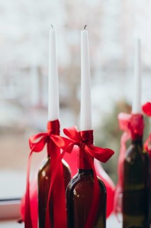 Elegant Valentine's Day decor featuring white tapered candles in wine bottles adorned with red