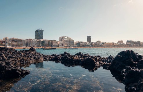 Tranquil cityscape view from volcanic rocks on a sunny day, showing modern buildings and calm