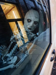 A haunting skeleton figure peers through a city window, its eerie reflection captured on the glass.
