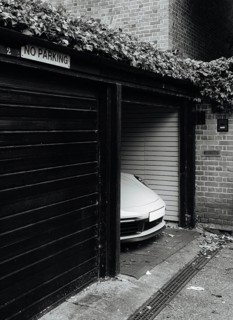 A sleek sports car is discreetly parked in a garage with a No Parking sign. The urban London