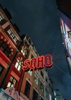 A vibrant neon Soho sign illuminates the street below, contrasting against a dark, moody London
