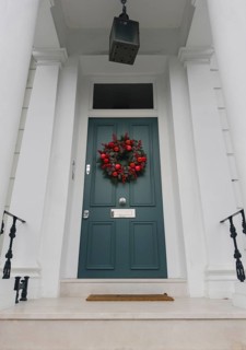 A stylish London doorway features a festive wreath with red ornaments, pinecones, and greenery