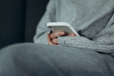 A person in a soft gray sweater holds a smartphone, reflecting a comfortable and relaxed moment.