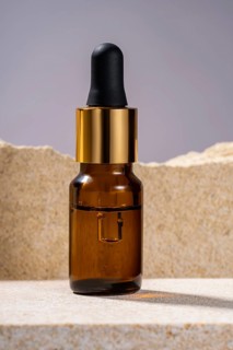 A stylish amber glass serum bottle with a black dropper and golden details, showcased on a textured