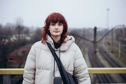 Young woman with red hair in a winter coat, standing on a bridge overlooking railway tracks in a