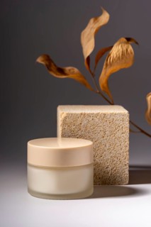 A sophisticated cosmetic cream jar displayed on a natural stone podium, complemented by artistic