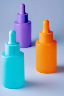A trio of vividly colored serum bottles in purple, orange, and teal, arranged aesthetically against