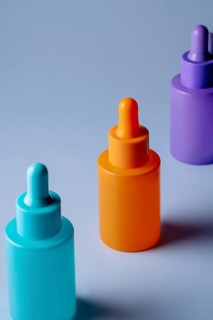 A set of brightly colored serum bottles in orange, purple, and blue against a soft blue background,