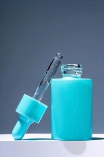 A striking image featuring a turquoise serum bottle with a glass dropper filled with liquid, set
