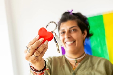 A joyful transgender woman holds keys and a heart lock, symbolizing a new beginning in her home. A