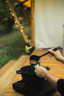 Cropped unrecognizable person pours spicy mulled wine into a mug, outdoors near twinkling lights