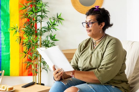 A trans woman enjoys a serene moment, sitting comfortably in her new home, reading a book. The
