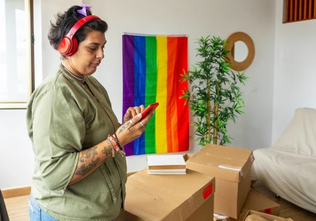 A transgender woman joyfully explores her new home, decorated with a rainbow flag symbolizing