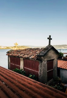 A traditional stone horreo granary with a cross atop its red tile roof overlooks a tranquil coastal