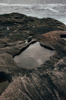 A serene coastal scene features rugged rock formations with shallow pools of water collected within