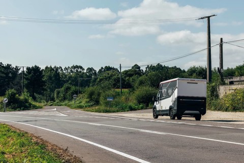A motorhome drives on a serene rural road surrounded by lush greenery and power lines under a clear