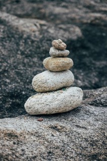 A stack of balanced stones sits on a rocky surface in a peaceful outdoor environment. The image