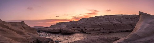Sweeping panoramic view of Sarakiniko beach on Milos Island, Greece, under a vibrant sunset sky.
