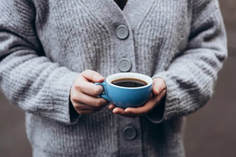 A person in a cozy gray sweater holds a blue cup coffee, capturing a peaceful moment of warmth and