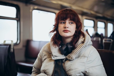 A thoughtful passenger with headphones sits on a train, gazing out of the window. The cozy winter