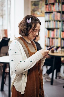 A young woman with a casual style checks her phone in a cozy bookstore. Surrounded by vibrant