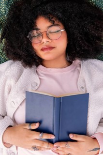 A peaceful latin woman in glasses rests with a book on a cozy day indoors. The scene captures