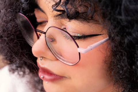 A detailed close-up shot of a latin woman wearing glasses. The focus highlights their piercings,