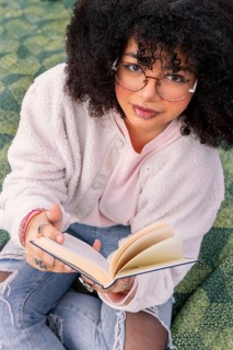 A young latin woman with glasses enjoys reading a book while sitting comfortably. Her casual style