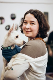 A young woman smiles warmly as she holds her adorable dog in a cozy bookstore. The pair share a