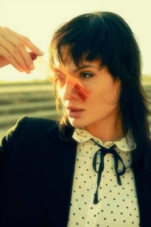 Woman holding a film strip against a sunlit background. She wears a polka dot blouse and black