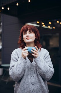 A young woman enjoys a coffee in a cafe terrace, wearing a cozy sweater, surrounded by string