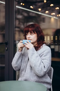 A young woman in a cozy sweater enjoys her coffee on a cafe terrace. The ambiance is warm, with a